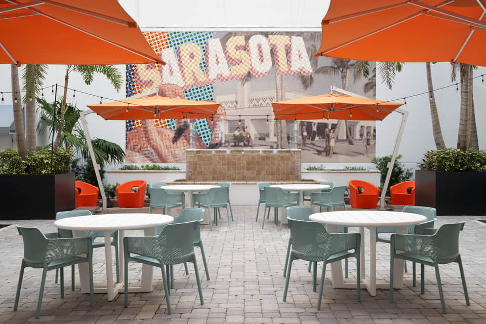 Outdoor patio seating area with orange umbrellas, mint green chairs, white round tables, and vintage pop art signage
