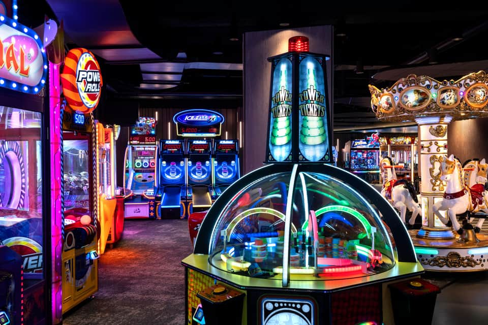 Colorful arcade game room with illuminated slot machines, racing games, and carnival-style games