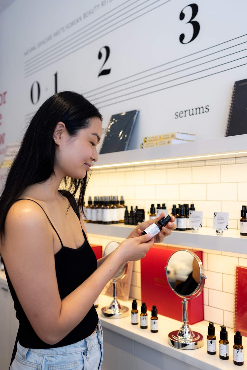 Woman examining serum product in modern spa retail display with numbered sections