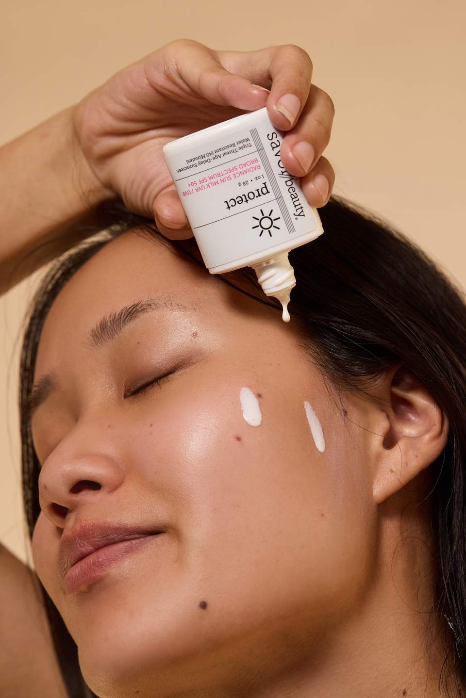 Person applying sunscreen lotion to forehead with product bottle