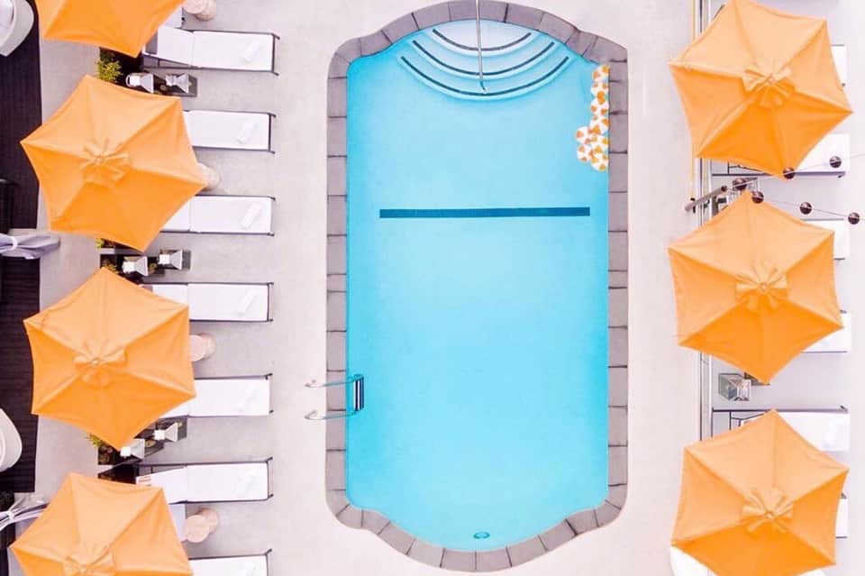 Overhead view of bright blue resort pool surrounded by orange umbrellas and lounge chairs