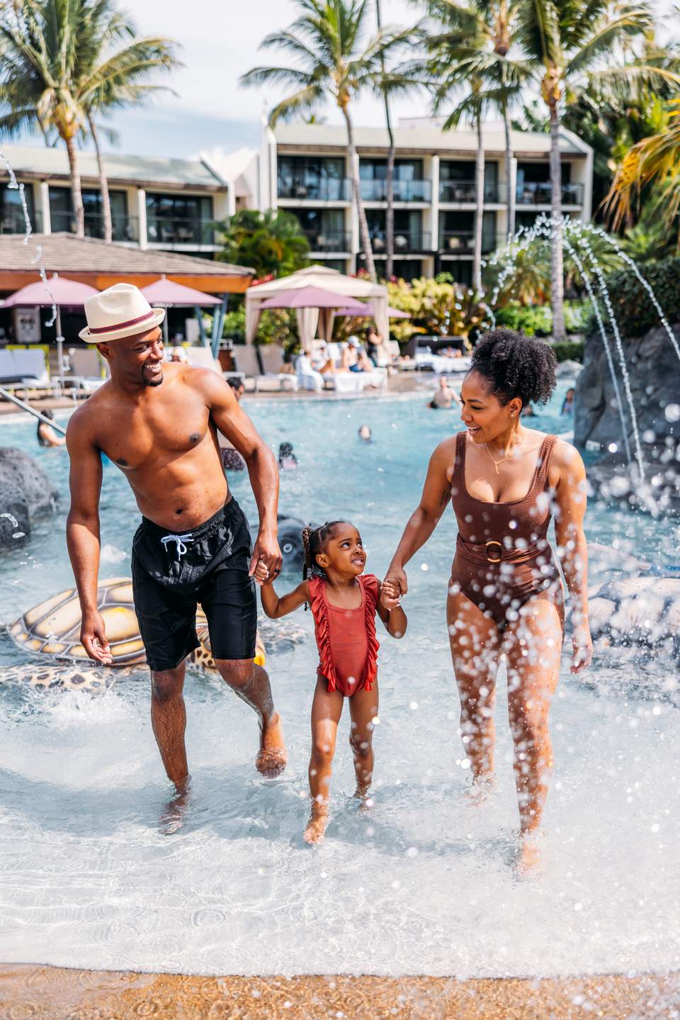 Family of three wading into calm ocean waters at a tropical beachfront resort