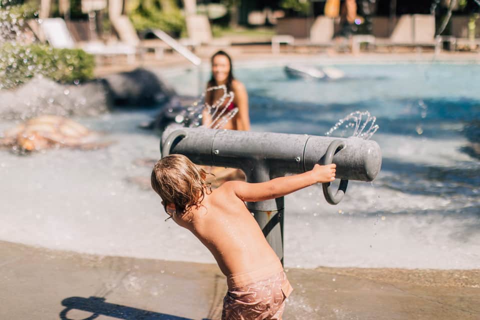 Child playing with a cannon toy on the beach while adult watches in background