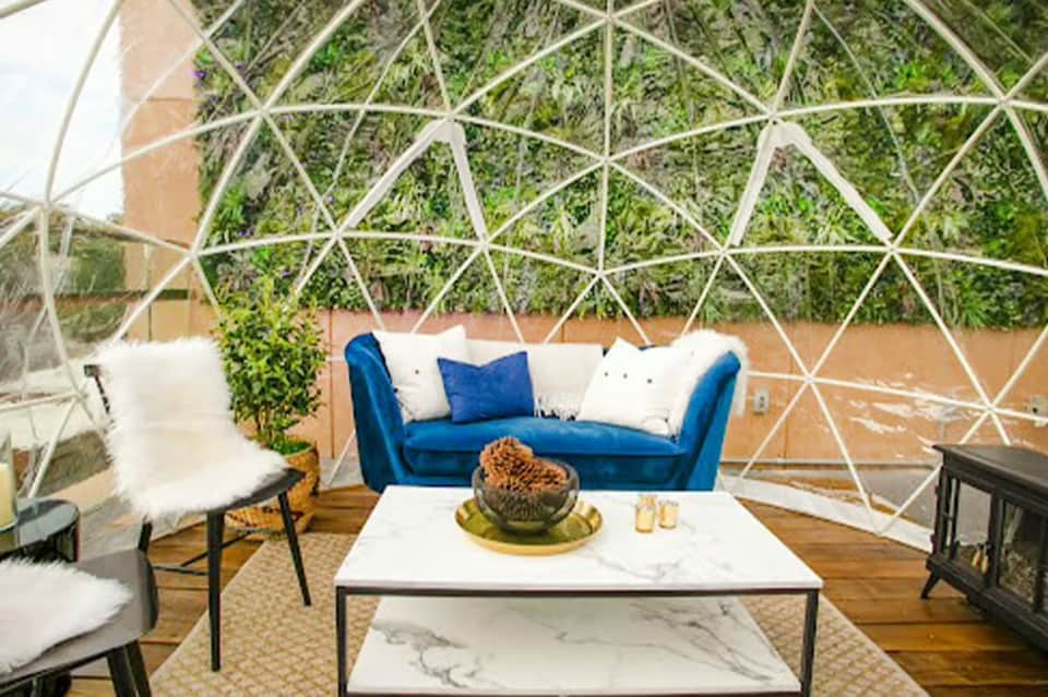 Modern geodesic dome interior with blue sofa, white chairs, and green living wall