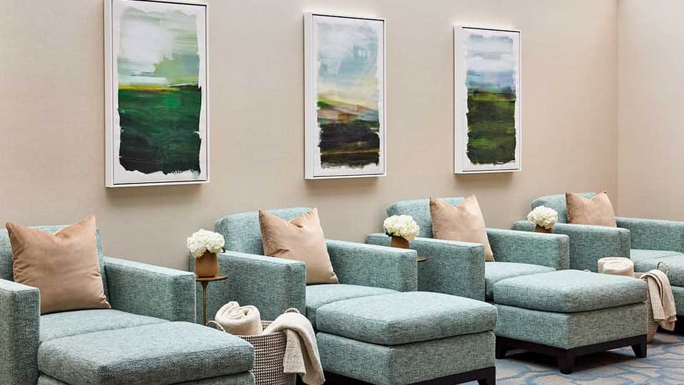 Spa lounge with turquoise upholstered seating, tan pillows, and framed landscape artwork on beige walls
