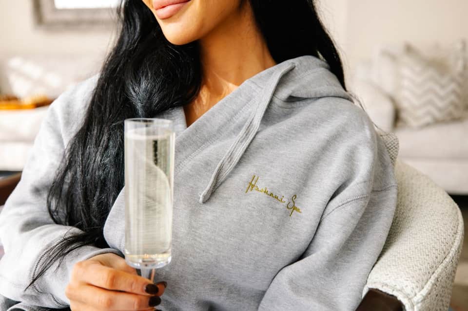 Woman in gray hoodie holding champagne flute, relaxing on neutral-toned seating