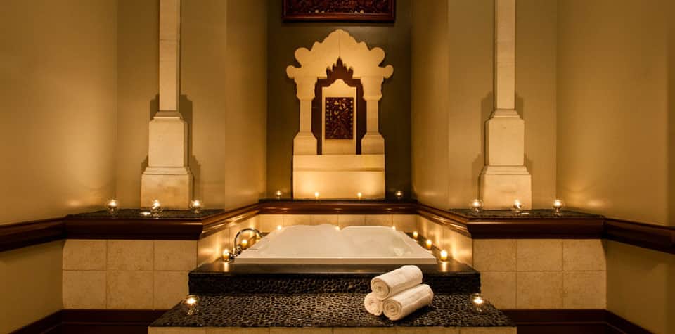 Luxurious spa bath with carved golden shrine backdrop and candle-lit stone surrounds