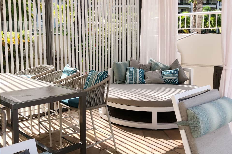 Modern balcony terrace with curved seating, striped awning, and coastal garden views through white railings