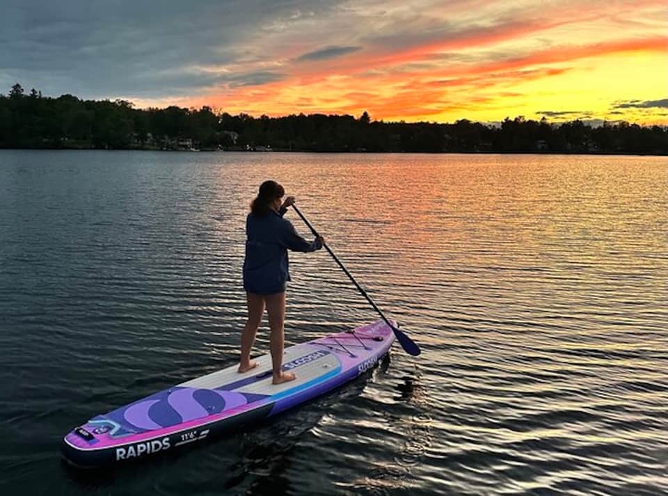 Woman stand-up paddleboarding on lake at sunset with colorful board