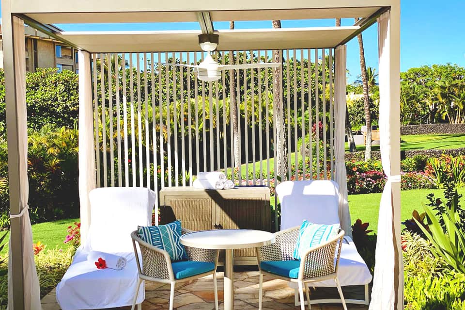 Shaded pergola seating area with wicker chairs, round table, and manicured garden landscape