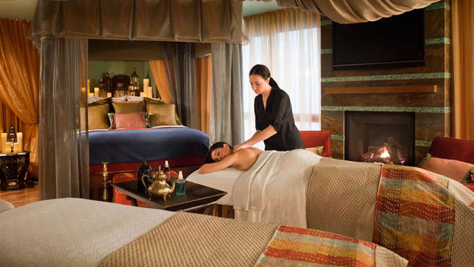 Spa therapist performing massage on client in luxury hotel room with fireplace and canopy bed