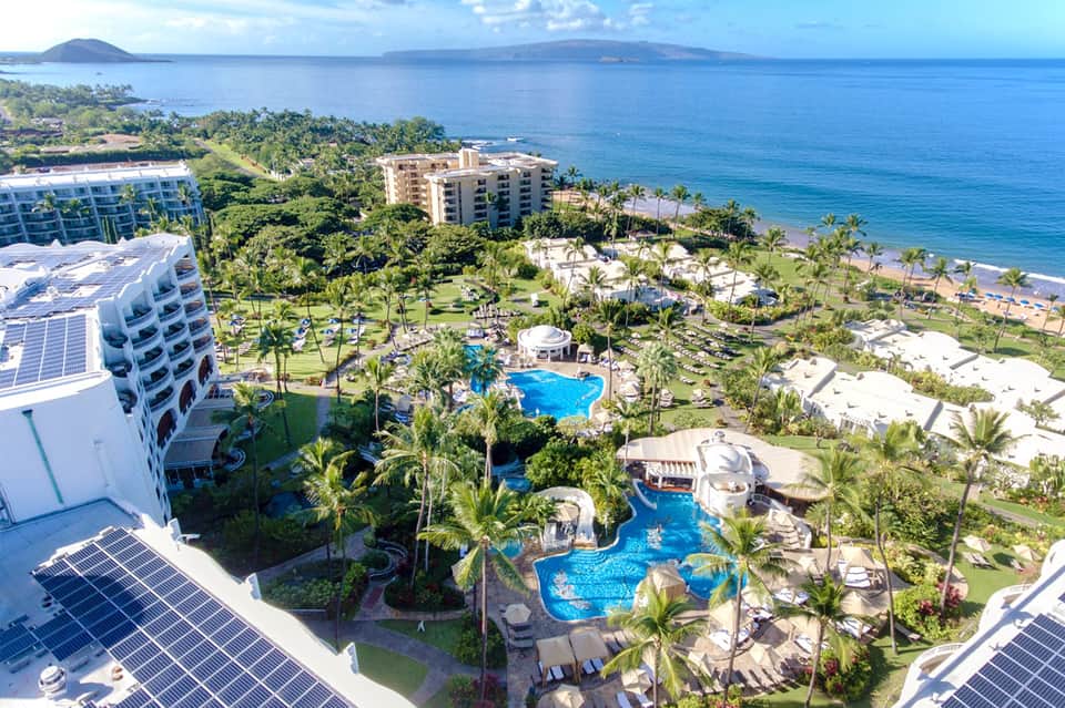 Aerial view of beachfront resort with multiple pools, palm trees, and ocean views