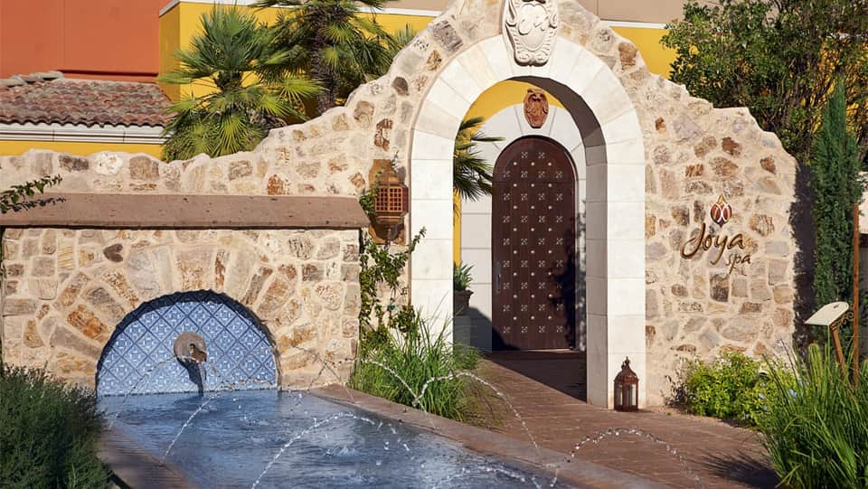 Stone spa entrance with ornate wooden door and blue mosaic water feature at resort