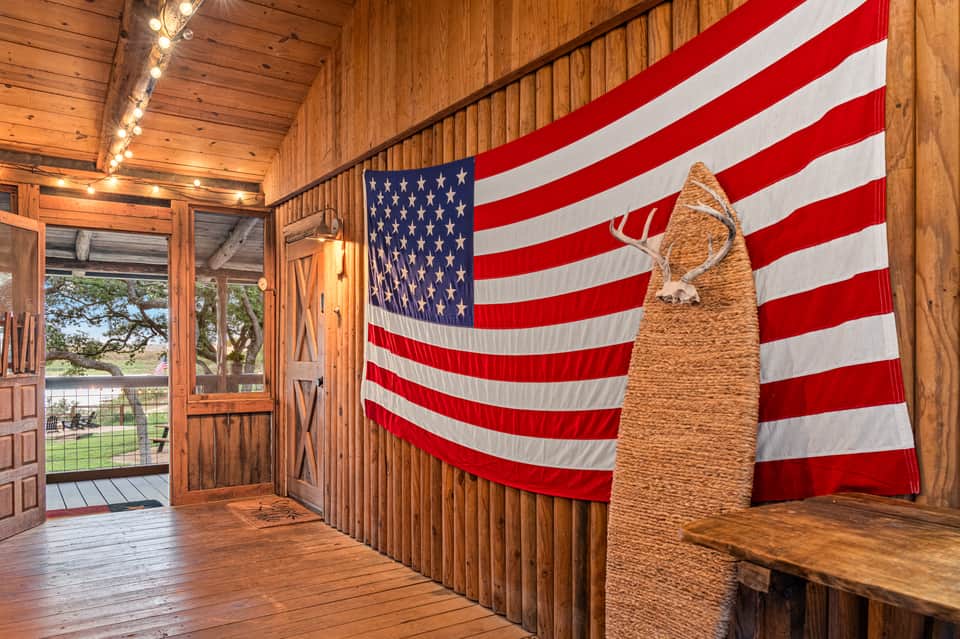 Wooden lodge interior with American flag display, deer sculpture, string lights, and open doors leading to outdoor deck