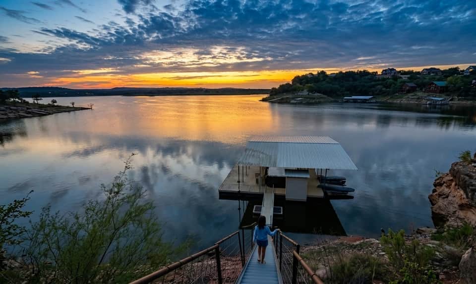 Serene sunset over a lake with a floating dock and residential area reflected in calm water