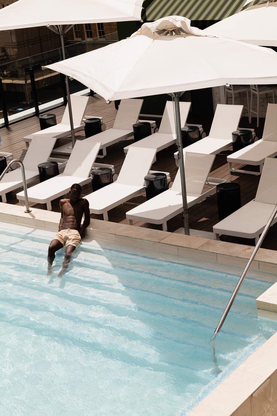 Man entering a resort pool with white lounge chairs and umbrellas on the deck in background