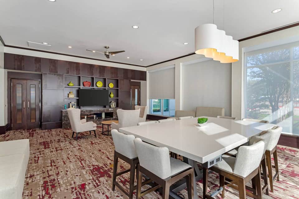 Modern dining and living space with white table, cream chairs, dark wood cabinetry, and large windows overlooking grounds