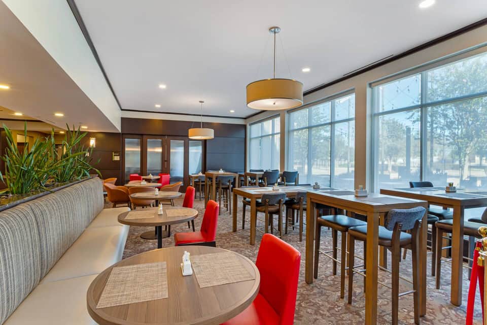 Contemporary lounge area with red accent chairs, round tables, large windows, and warm lighting from pendant fixtures