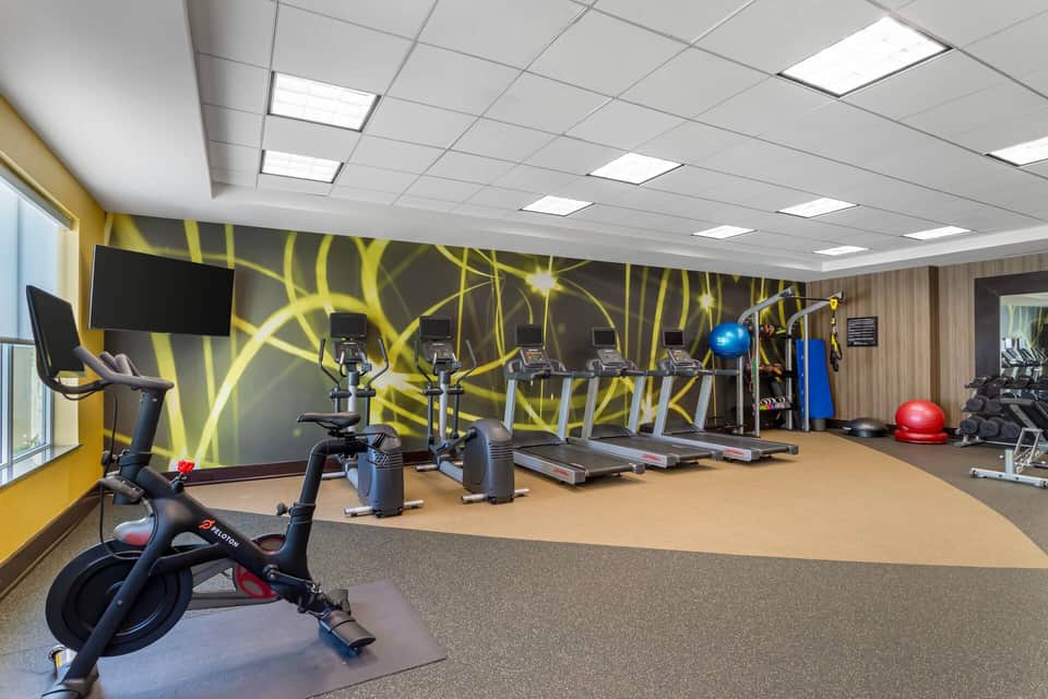 State-of-the-art fitness center with cardio equipment, yellow accent wall, and mirrored surfaces