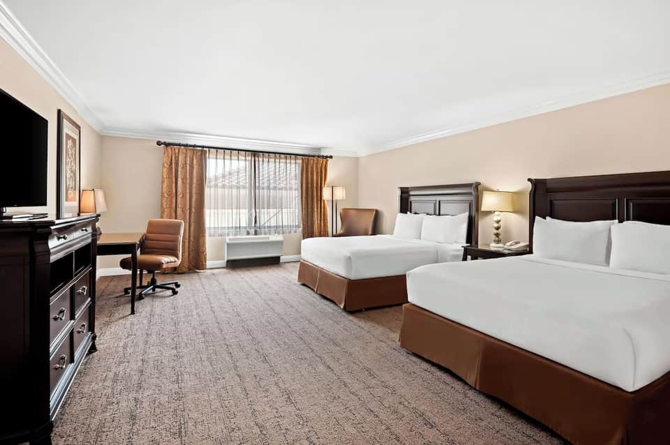 Hotel guest room with two queen beds, dark wood furniture, brown bedding, and sitting area