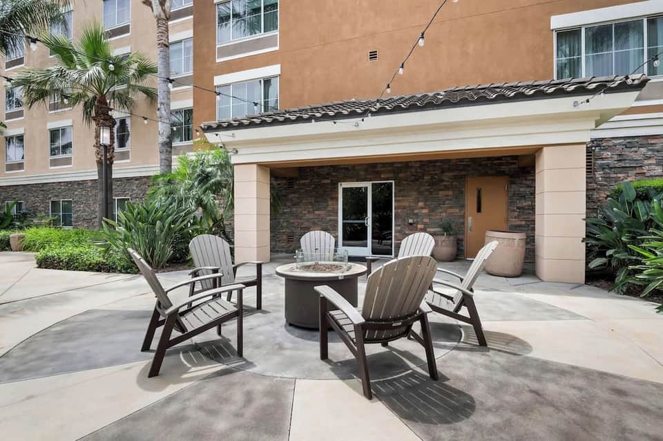 Outdoor patio with fire pit, Adirondack chairs, palm trees, and modern hotel building exterior