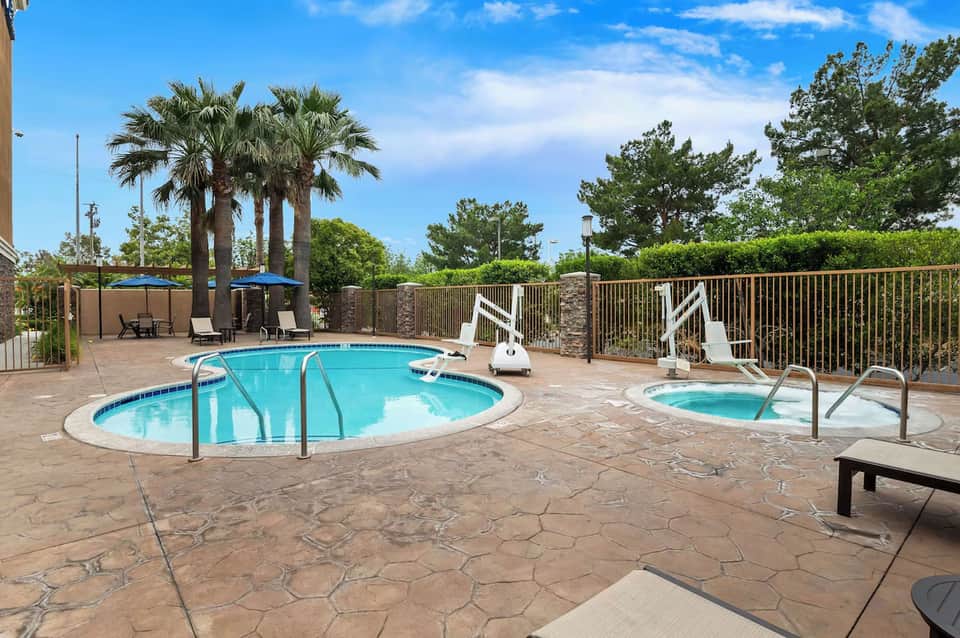 Resort pool and spa area with palm trees, lounge chairs, metal railing, and sunny landscaping