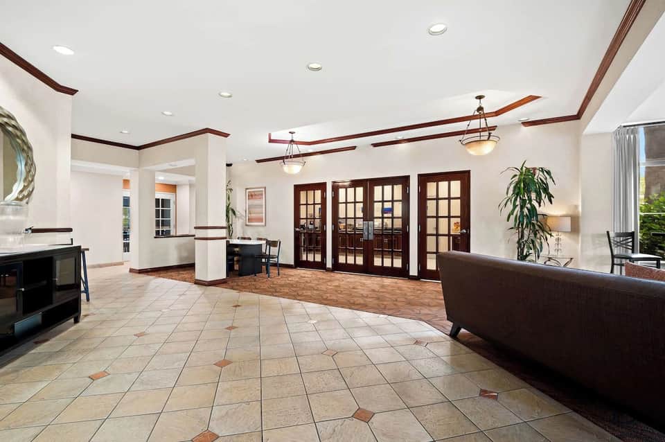 Spacious hotel lobby with tile flooring, dark wood beams, French doors, fireplace, and contemporary furnishings