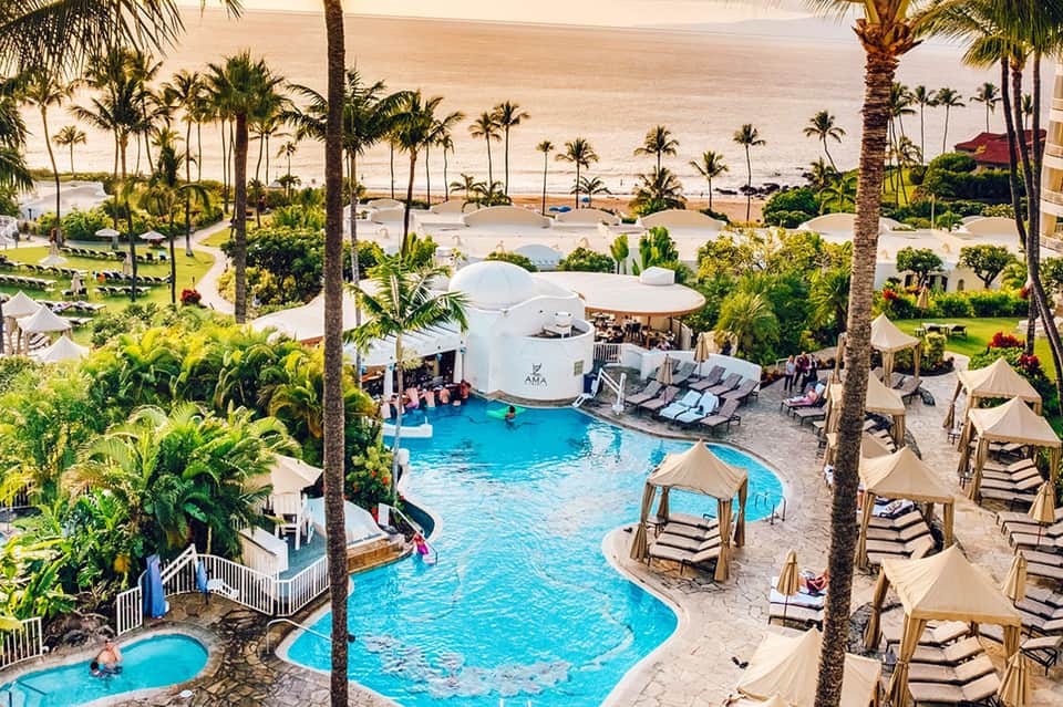 Aerial view of beachfront resort with multiple pools, palm trees, and ocean shoreline