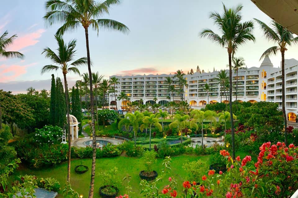 Luxury beachfront resort at dusk with palm trees, lush gardens, and illuminated white architecture