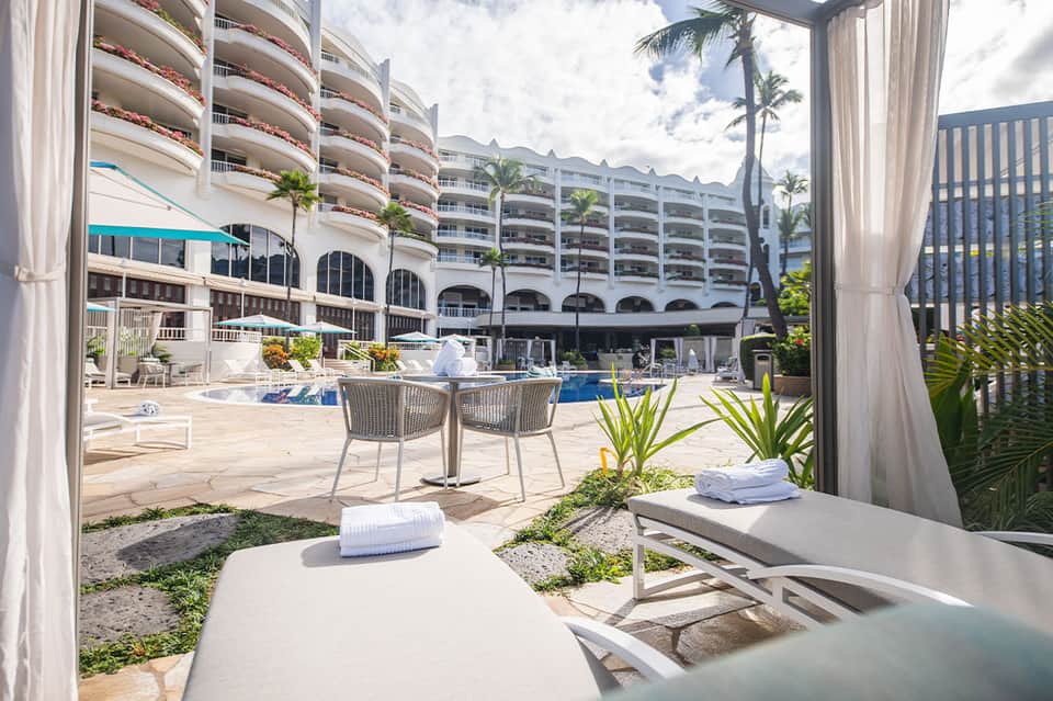 Resort courtyard with lounge chairs, pool, and multi-story white hotel building with palm trees