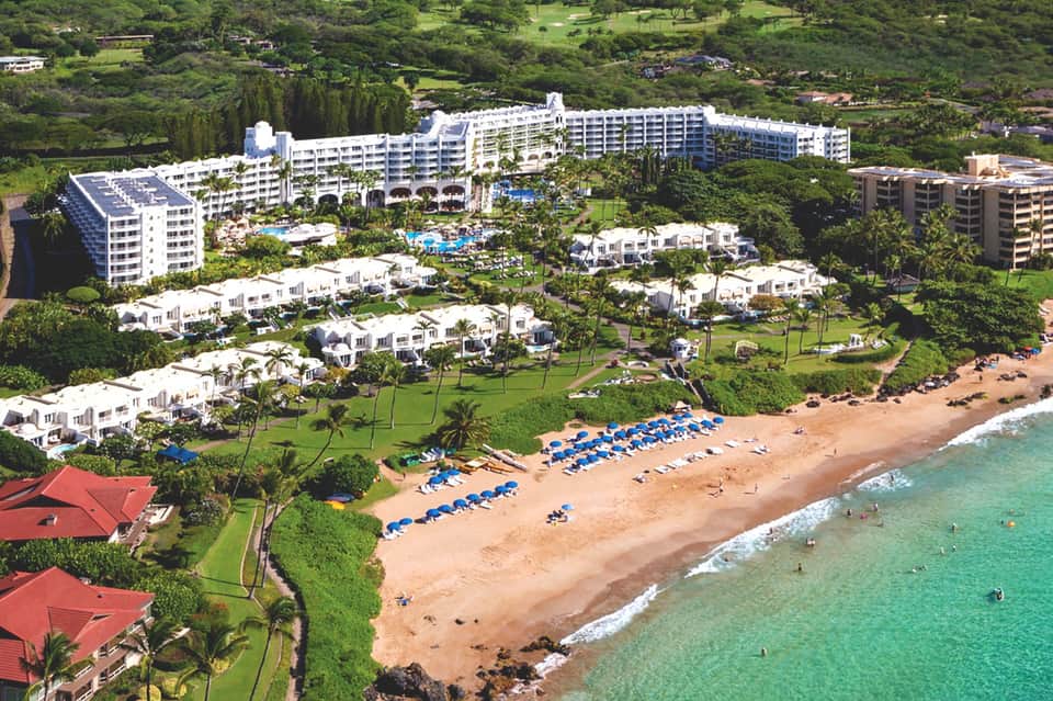Aerial view of beachfront resort with white buildings, manicured grounds, and turquoise ocean