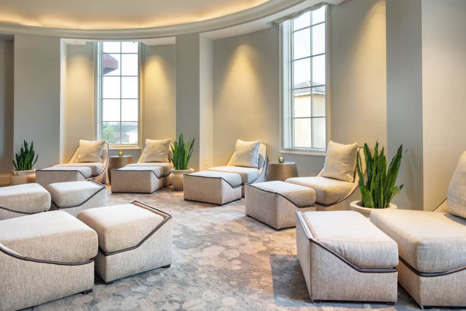 Modern spa relaxation room with beige seating, natural lighting, and potted plants