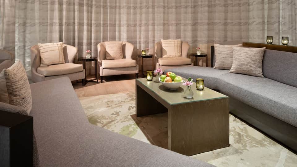 Luxury lounge with beige wingback chairs, gray sofa, wooden coffee table, and soft ambient lighting