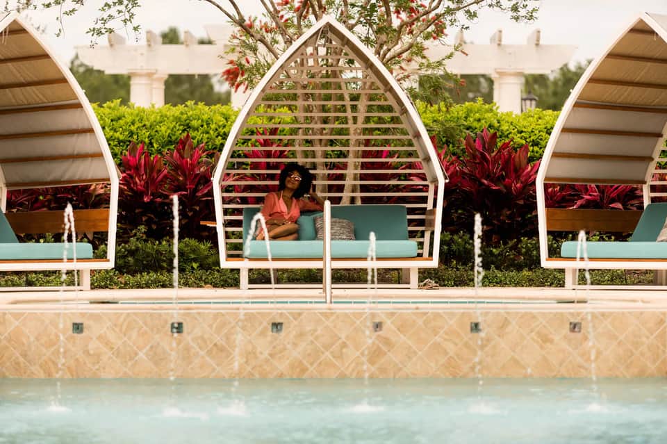Outdoor pool cabanas with white lattice design and green cushioned seating by turquoise water