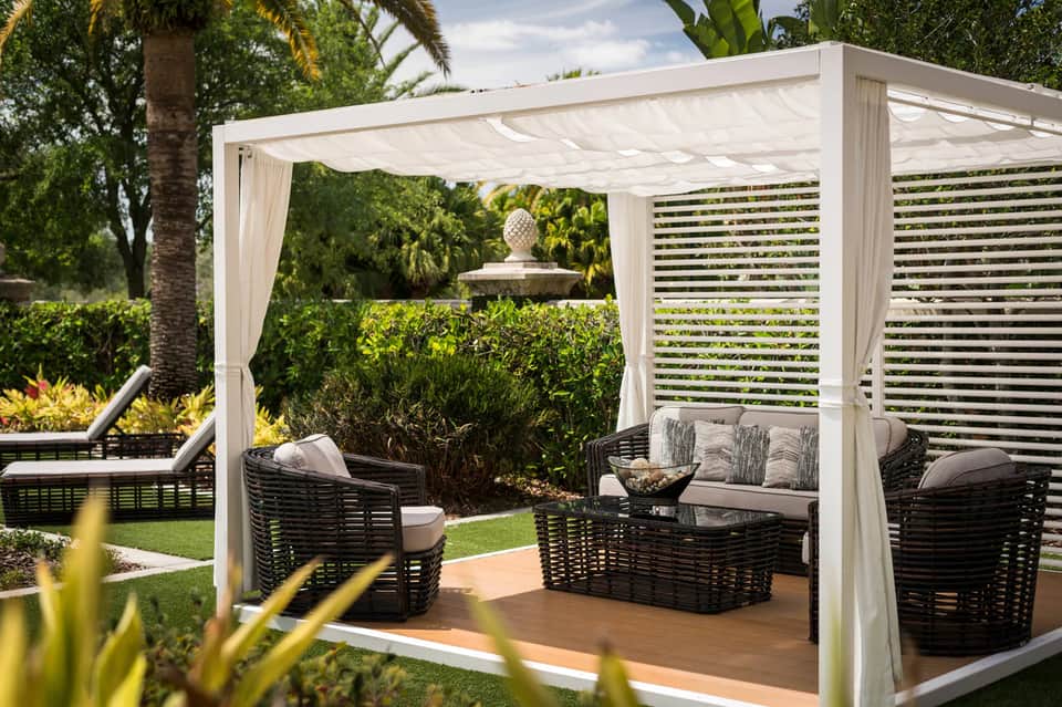 Modern pergola seating area with black wicker furniture, white curtains, and manicured landscaping