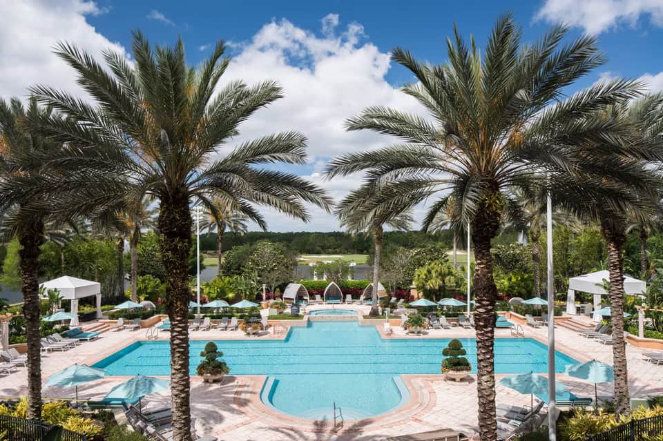 Resort main pool surrounded by palm trees, white umbrellas, lounge chairs, and turquoise water
