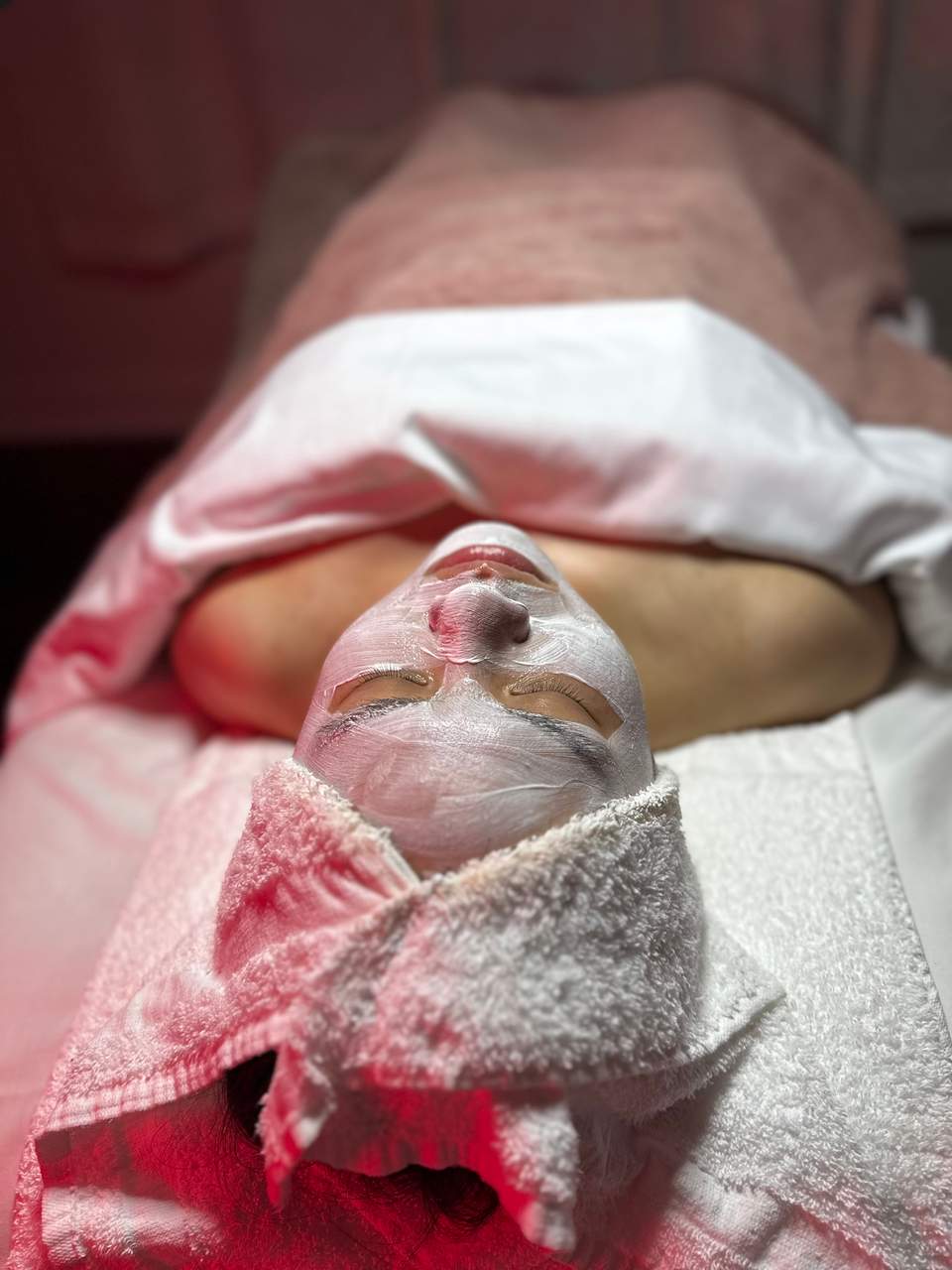 Close-up of client's face with white spa treatment mask applied, relaxing on massage table