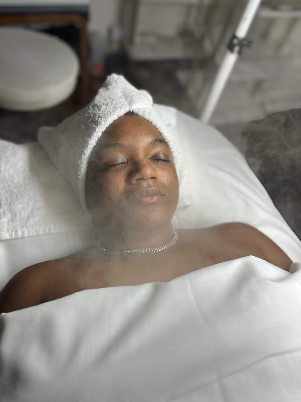 Client with towel wrap and headband lying on spa bed during facial treatment session