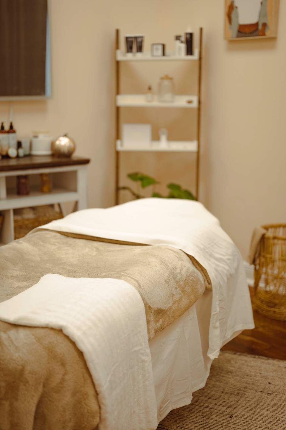 Minimalist spa treatment room with beige walls, wooden shelving, vanity, and massage bed