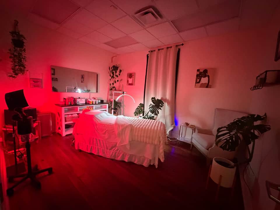 Full spa treatment room with red neon lighting, massage bed, vanity, plants, and modern décor