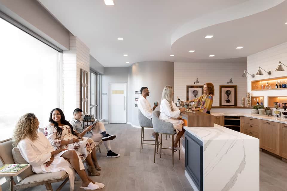 Modern hotel spa lounge with guests relaxing, marble counter, wood cabinetry, and contemporary pendant lighting