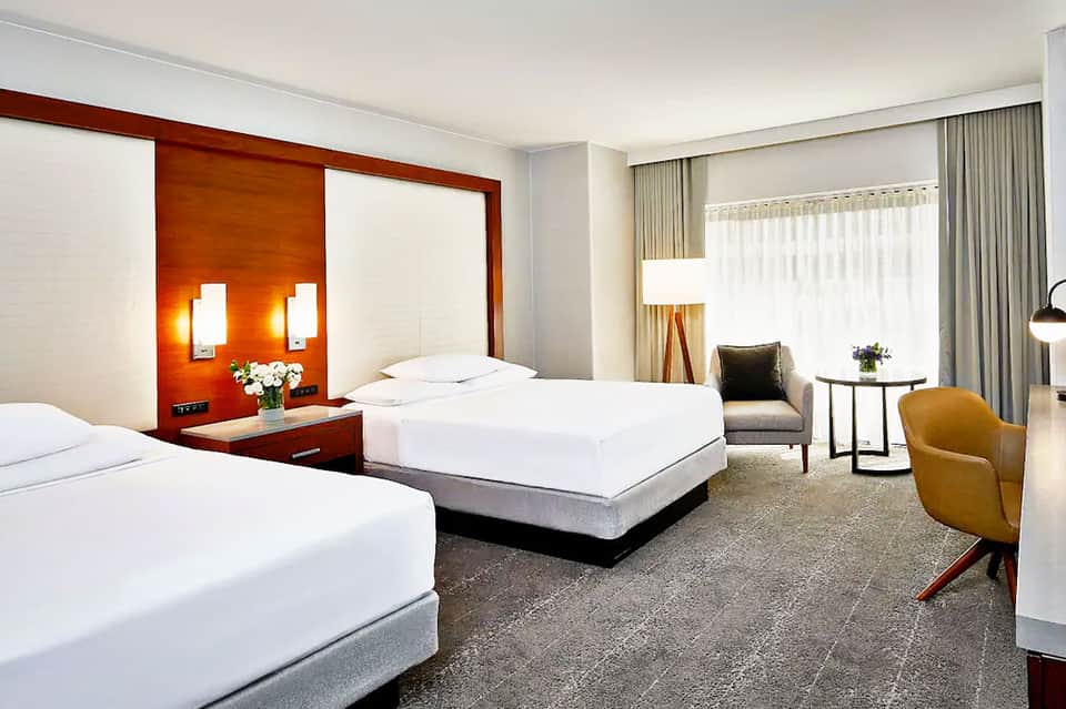Modern hotel room with two beds, orange accent wall, and contemporary furnishings