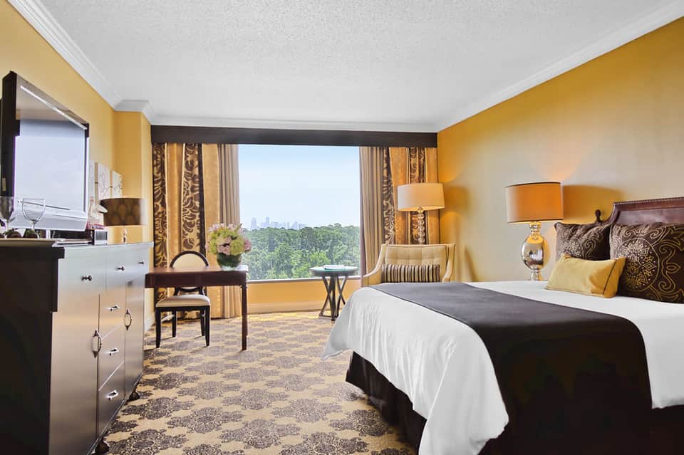 Luxury hotel bedroom with yellow walls, city views, dark wood furnishings, and elegant bedding