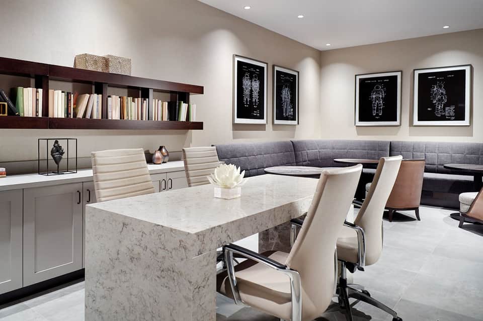 Modern lounge area with gray sectional sofa, marble dining table, bookshelves, and framed artwork