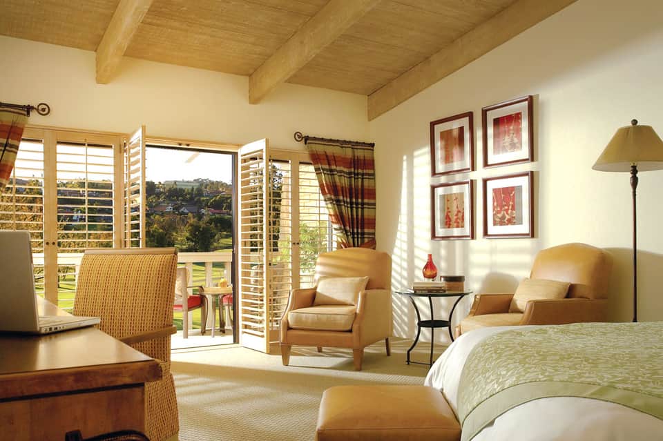 Luxury bedroom with wooden ceiling beams, balcony view, seating area, and warm earth tones