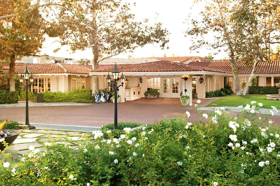 Spanish colonial-style resort courtyard with terracotta tile roofing, white columns, brick paving, and white flowering plants