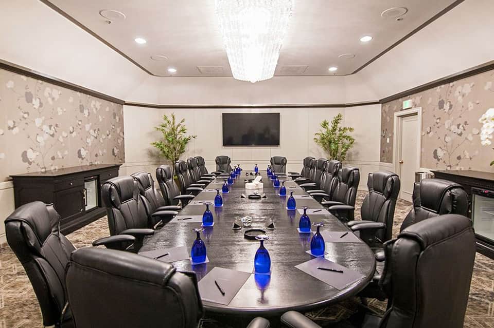 Formal conference room with long oval table, black leather chairs, and wall-mounted TV