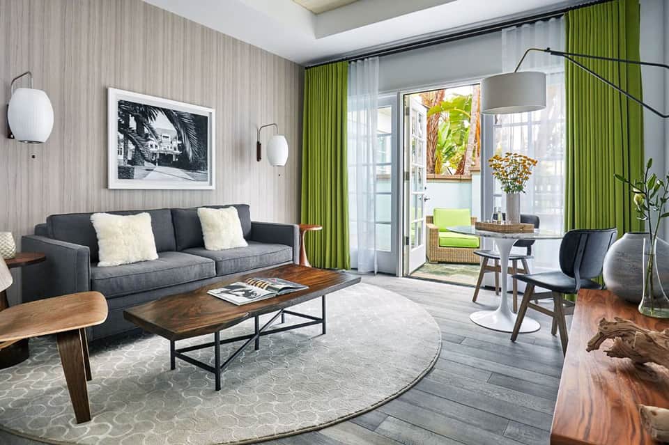 Modern living room with dark gray sofa, round area rug, wooden coffee table, and floor-to-ceiling windows opening to a balcony