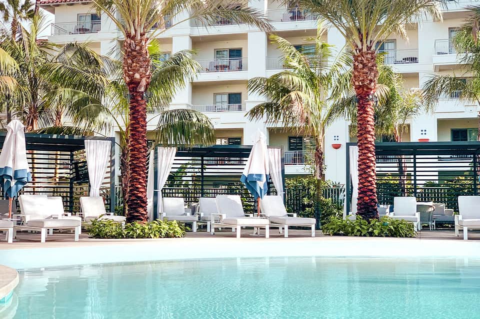 Luxury resort poolside with white loungers, palm trees, and modern white building with balconies