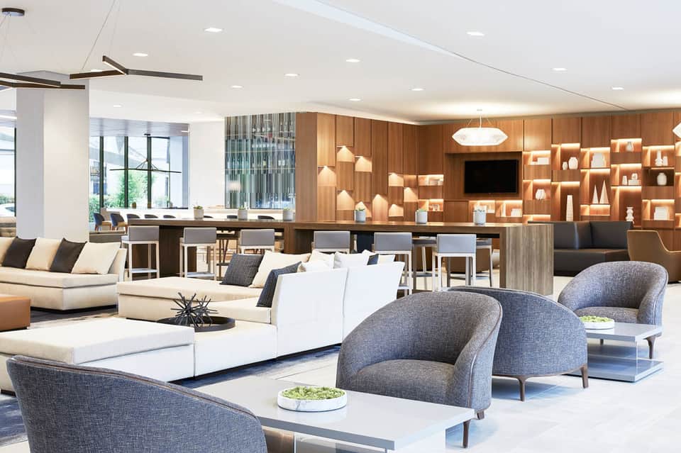Modern hotel lobby with contemporary furniture, wooden shelving, and bar seating area